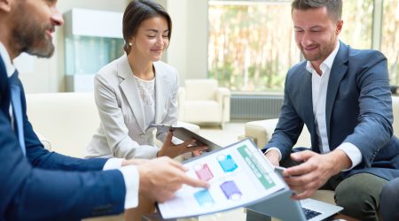 Group of cheerful business people working together during meeting in modern office, using laptop and planning marketing strategy