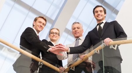 We are the best. Low angle view of four confident business people standing close to each other and holding hands together